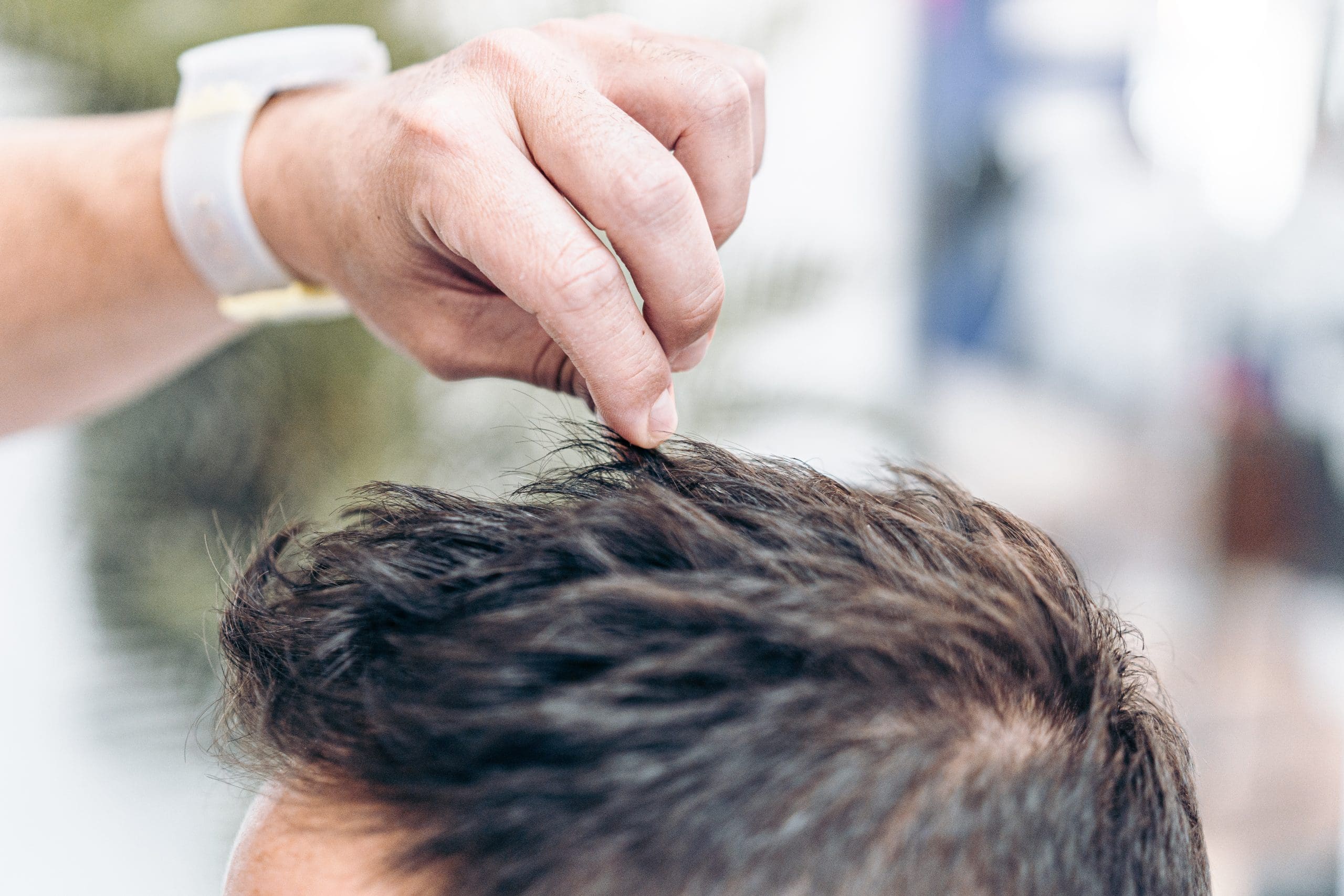 Close up view of the hand of a barber fixing the hair of a Caucasian client with hair gel